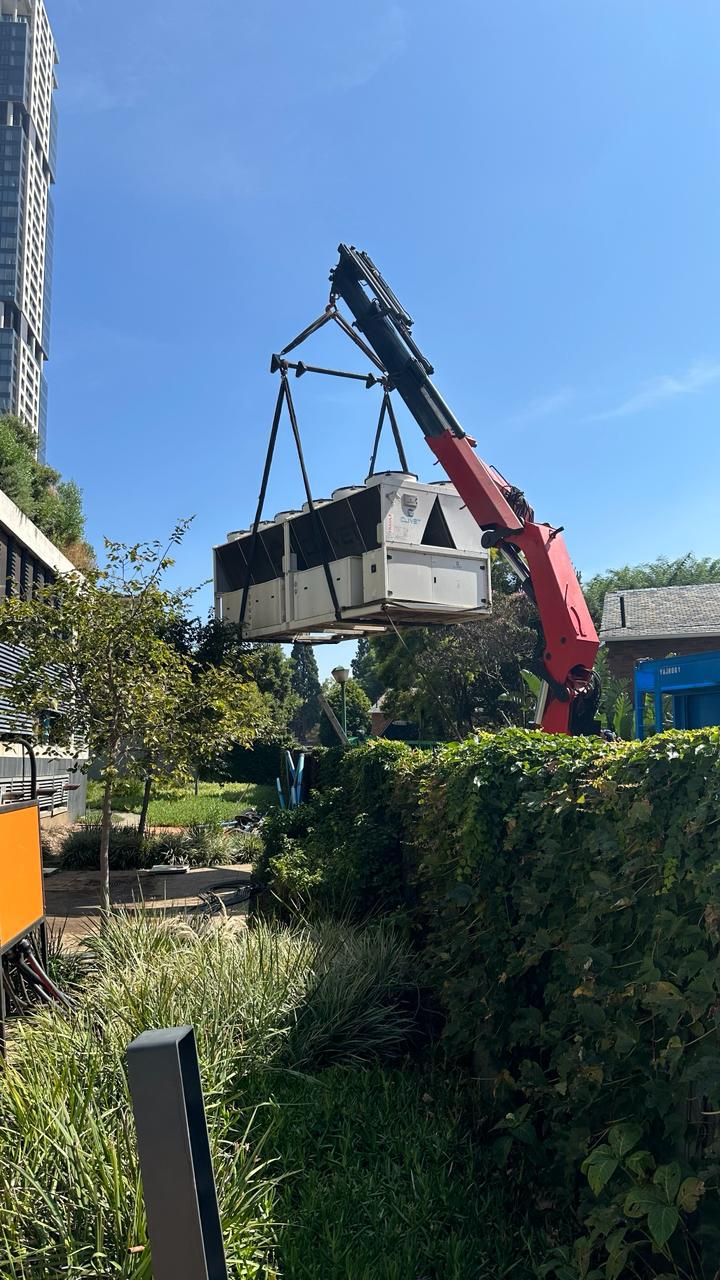 Crane lifting a rooftop package unit over landscaping on site