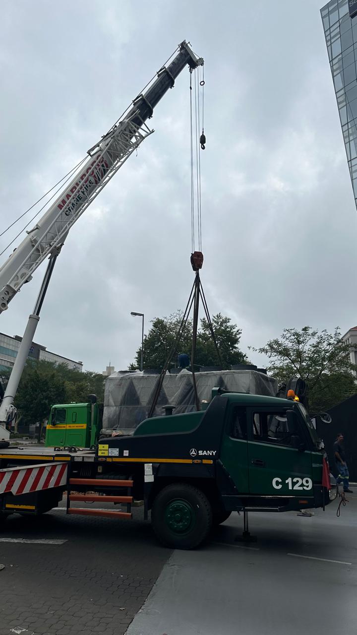 Mobile crane lifting a cooling tower off a truck at a commercial site