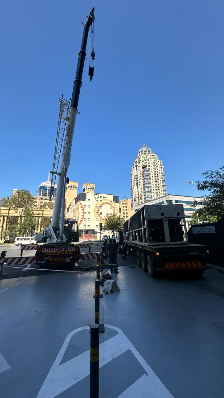 Mobile crane hoisting a large packaged unit off a truck