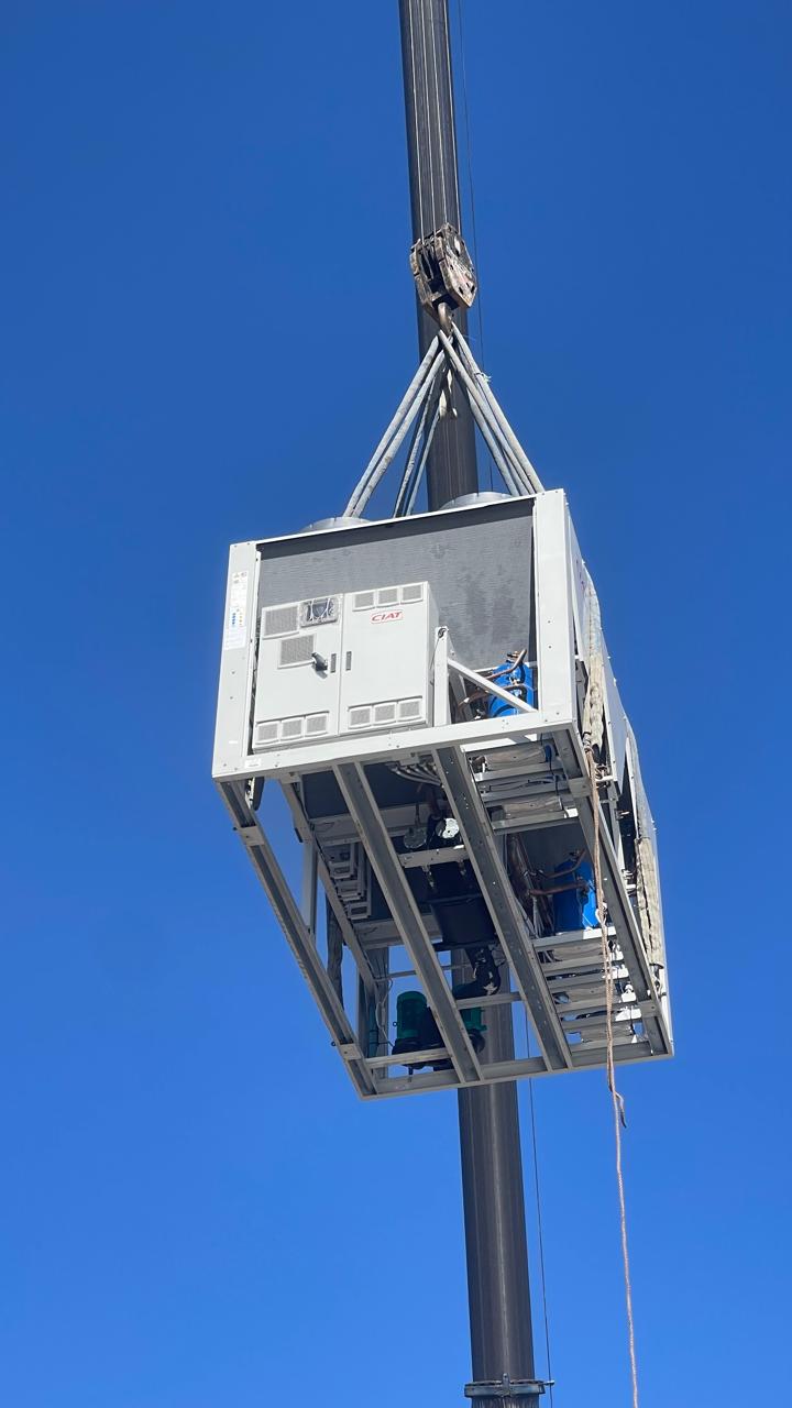 Packaged rooftop unit suspended from a crane against a blue sky